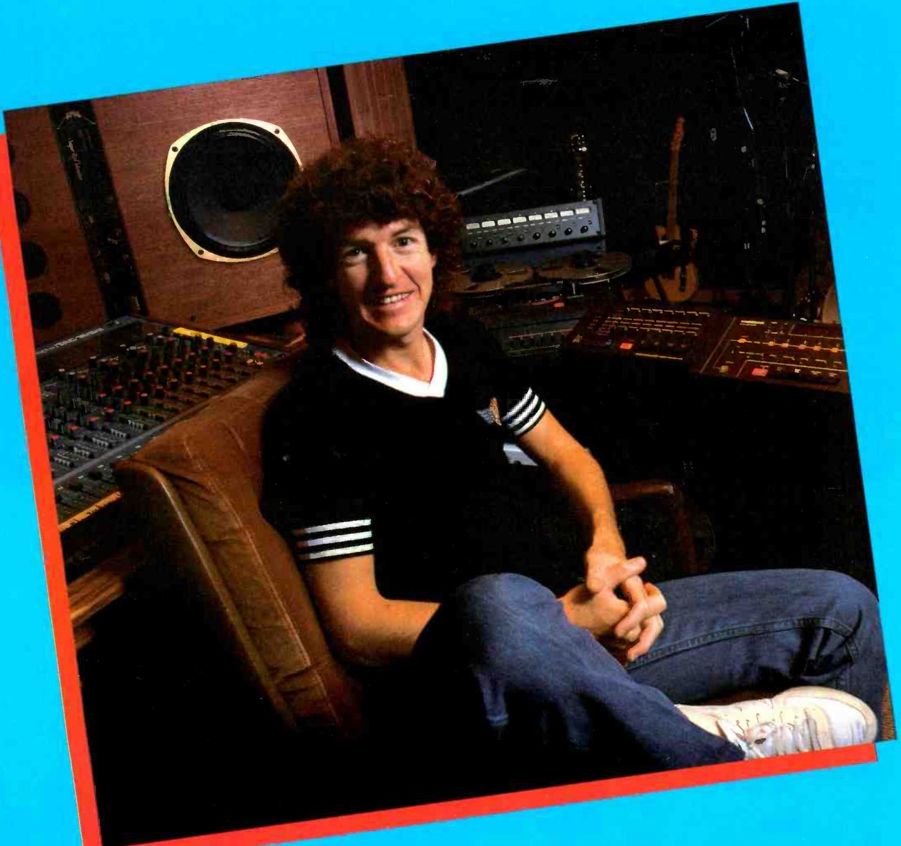 Kevin Cronin seated in a leather chair in his studio, in a tilted photograph with a red border: a mixing console at the left behind him, a monitor loudspeaker in a wooden wall, and over his shoulder a MARK III/8 with its eight-channel meter bridge and reels, beside a pair of rack units.