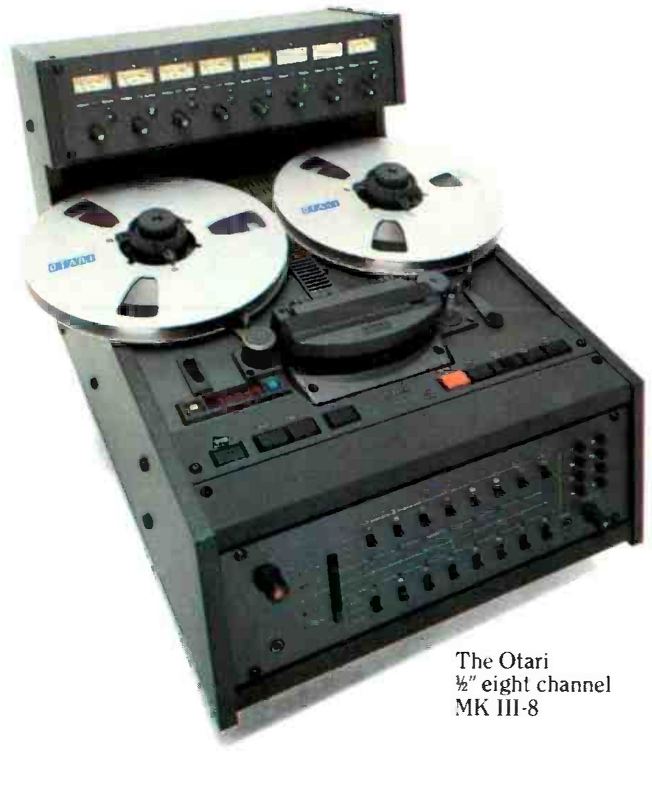 The MK III-8 photographed from a three-quarter angle: the meter bridge of eight meters and knobs across the back, two Otari reels on the flat transport, the head block and transport buttons, and the channel electronics on the sloping front panel below.