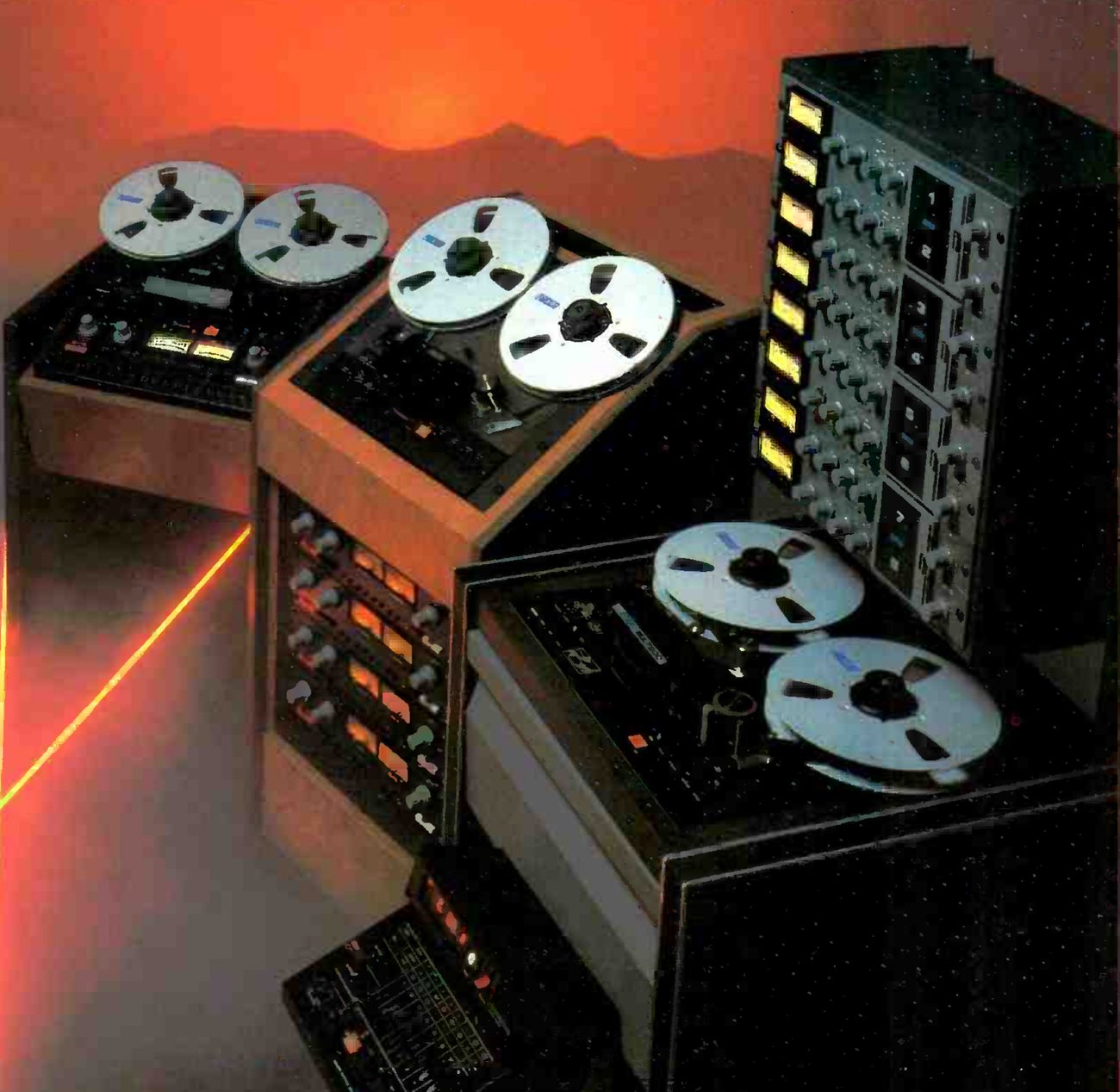 Detail of the three recorders: at left a two-channel machine set flat in a wooden console, beside it an eight-channel half-inch machine in a taller wooden console with four rows of paired meters below the transport, and at right a larger machine with a separate tall meter bay and a remote control unit in front.