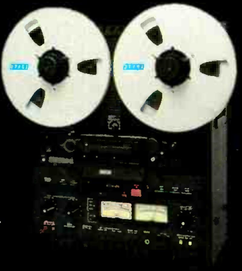 The MX-5050B-II photographed head-on against a black ground: two large reels with blue labels on the flanges above the transport, the pair of VU meters on the electronics panel below, and the cabinet side visible at right.
