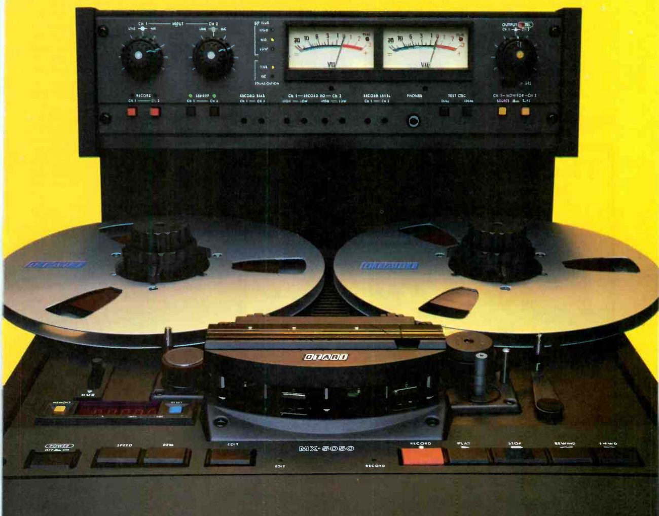 The MARK III-2 photographed close from the front: the meter bridge with two VU meters, input and output level knobs and rows of calibration controls, two OTARI reels on the transport, the head assembly under its OTARI-badged cover, and the transport pushbuttons along the front edge with MX-5050 lettered at the centre.