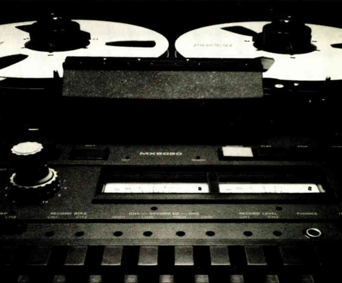 A close, low-angle photograph of the MX-5050B's faceplate: the reels behind the head cover, the MX5050 legend above the two VU meters, the recessed record bias, record EQ and record level trimmers along the lower panel with the phones jack at right, and the ribbed foot of the case.