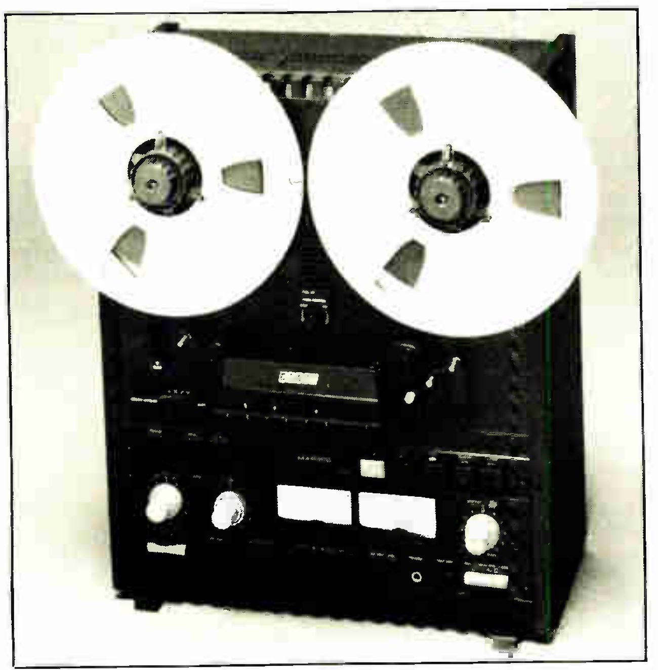The MX-5050B photographed against a white backdrop: two reels, the head cover and transport keys, a pair of VU meters between the input and output level knobs, and the ribbed foot of the black case.