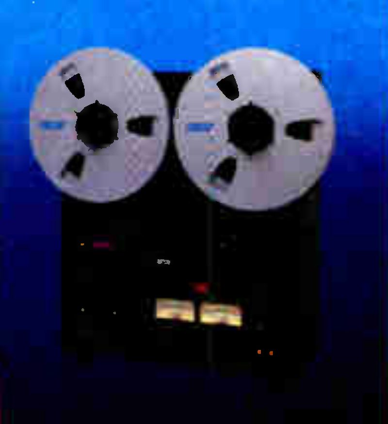 The MX-5050B-II photographed head-on against a blue ground: two silver reels above a black transport and electronics panel with a pair of lit VU meters.