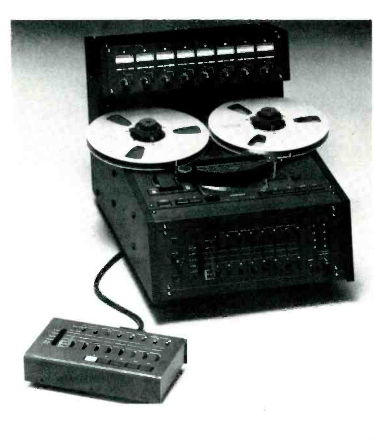 The MARK III/8 photographed from a high three-quarter angle on a pale ground: a meter bridge of eight meters with a knob under each across the back, two metal reels on the flat transport, the transport buttons and the sloping front panel of channel switches below, and the remote control unit in the foreground on its cable.