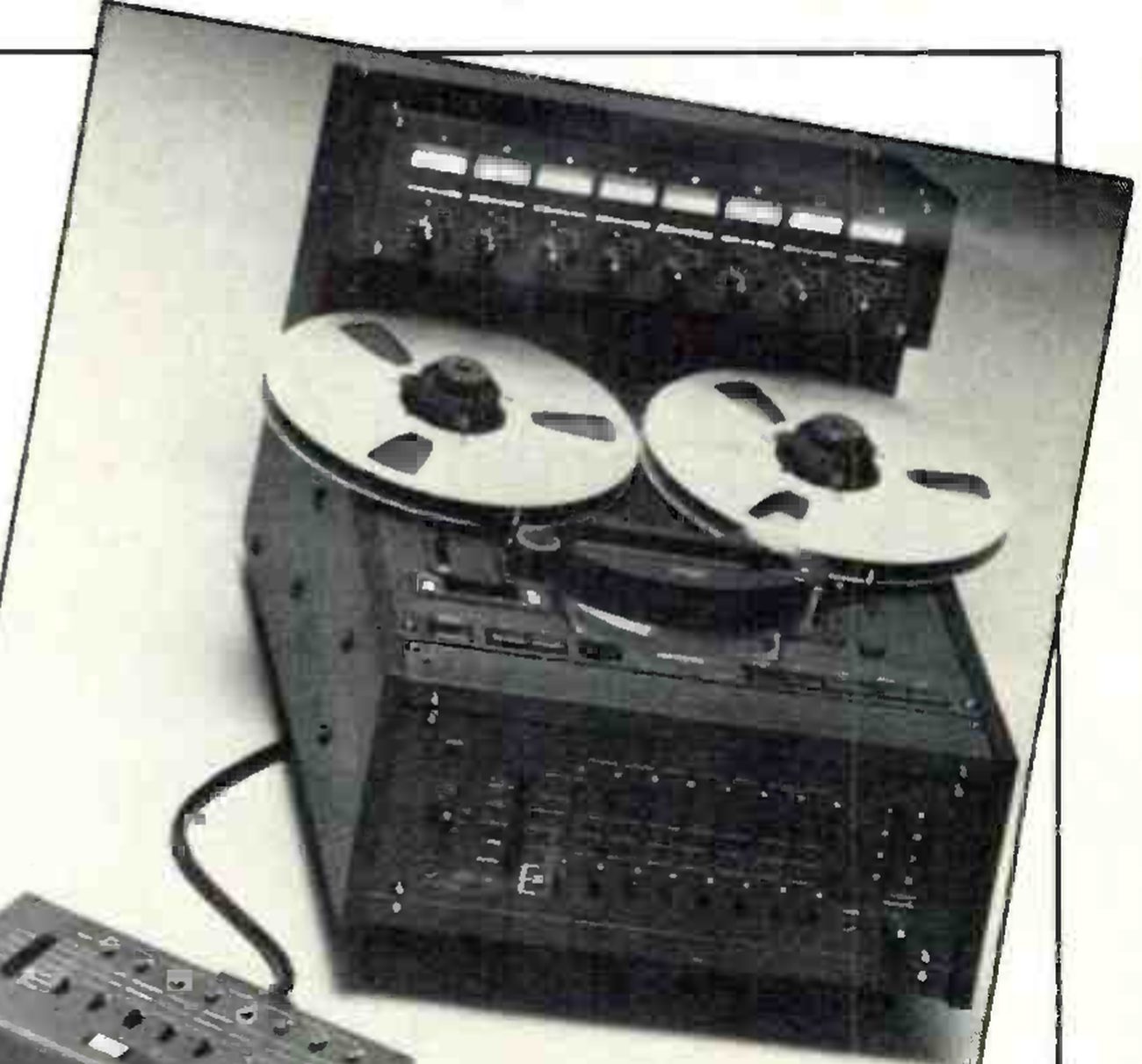 The MARK III/8 in a photograph set at a tilt: the desk-top cabinet with two large reels on the sloping transport, the eight-channel meter bridge above, the channel controls across the front panel, and a cabled remote unit in the foreground, its left end and lower half cut off by the crop.