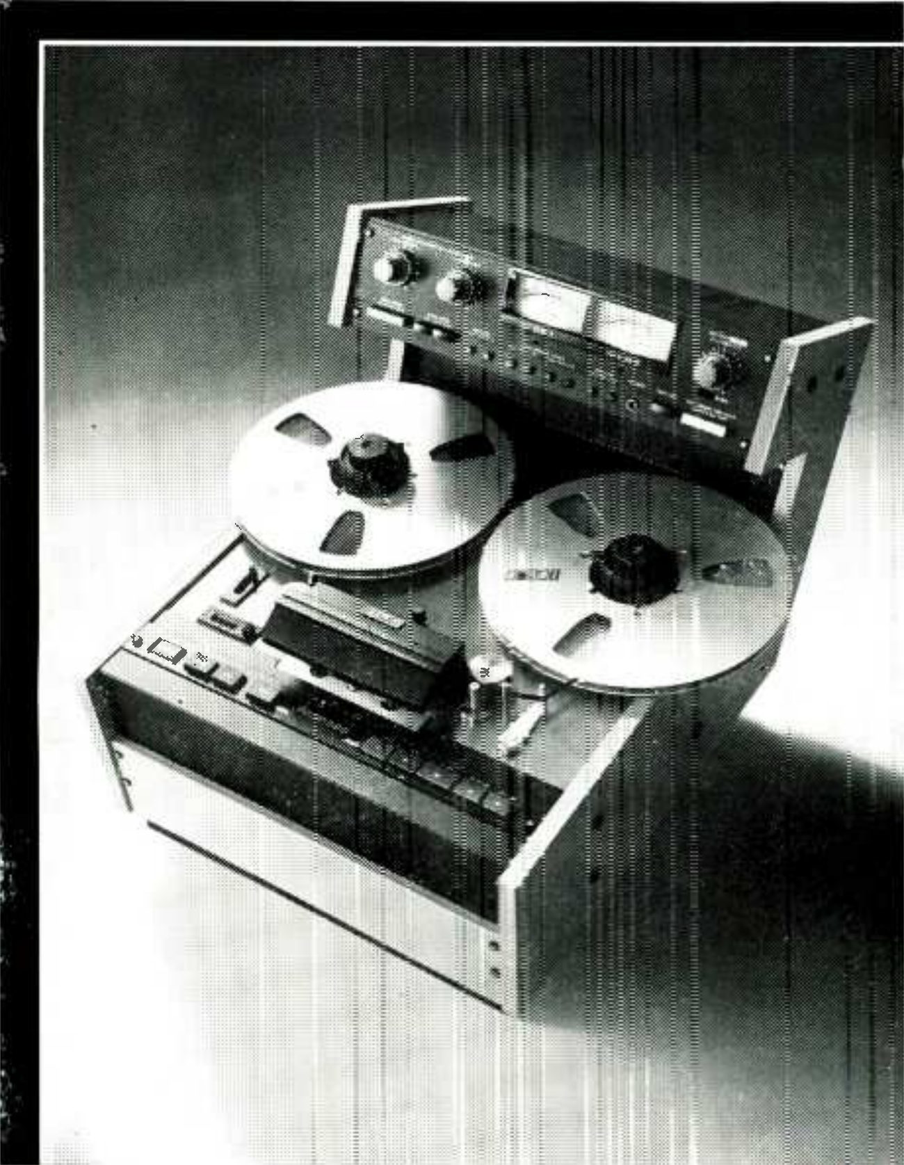 The MX5050 MK II-2 photographed from above at a steep angle against a ground that fades from dark grey to white: two reels on the transport, the head assembly under its cover and the row of transport buttons along the front, the whole deck in a cabinet with light-coloured side cheeks, and the separate electronics unit standing up behind it with two VU meters and its level knobs.
