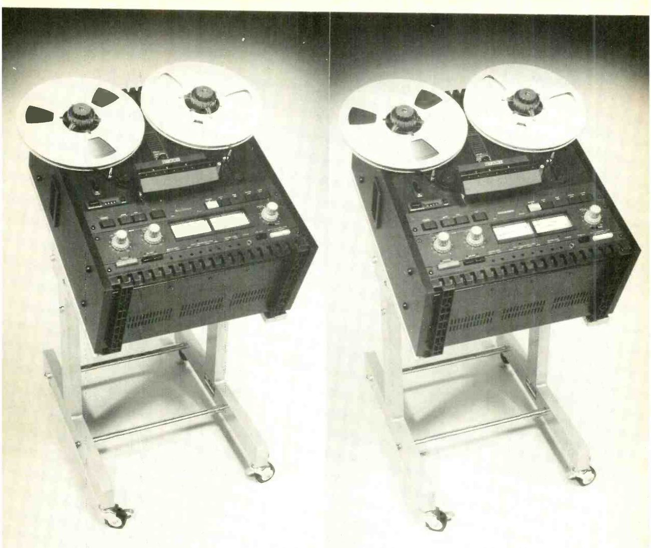 Two identical MX5050B machines side by side, each mounted tilted back on a tubular metal floor stand with casters: reels on the transport, the head cover, the meter bridge with its two meters, and the row of keys along the front of the electronics.