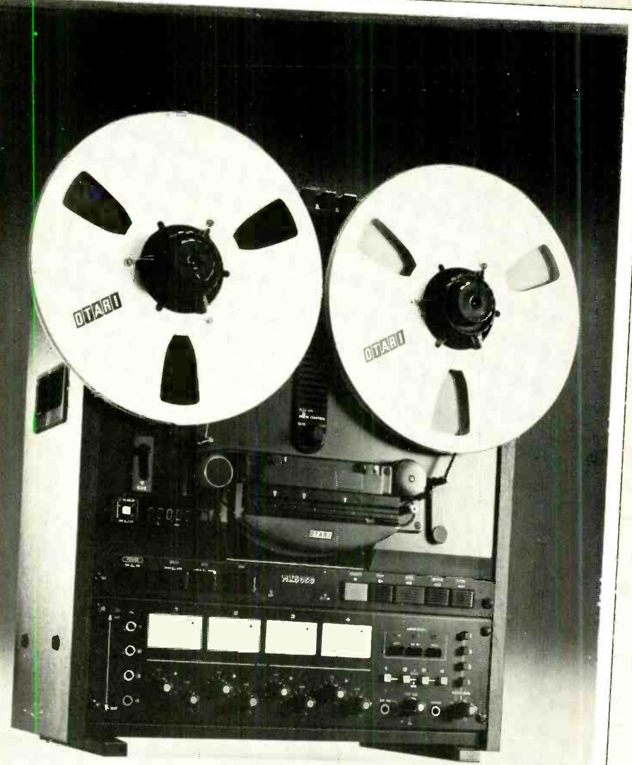 The MX5050 BQII photographed from the front in a large framed print: two reels with OTARI on the flanges, the head assembly under its cover with an OTARI badge, the LED tape counter at left of the transport, the transport buttons beneath, and four rectangular VU meters in a row on the electronics panel with the channel controls below.
