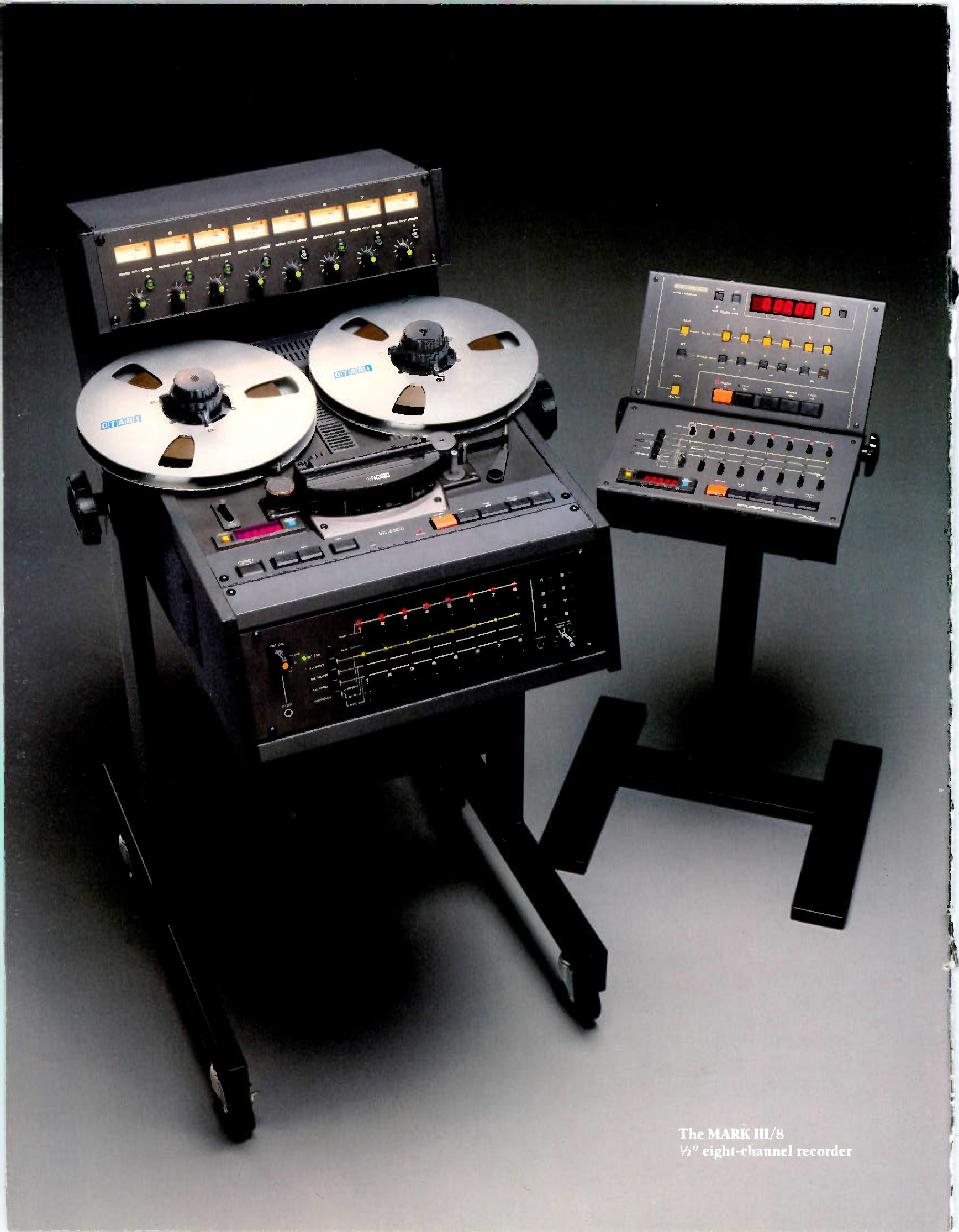The MARK III/8 on its roll-around floor stand: the eight-channel electronics in a rack unit at the top, two white NAB reels on the transport below them, the meter bridge and its LED ladders across the front of the machine, and the CB-110 remote session controller on a second stand at the right, the whole on castered legs.