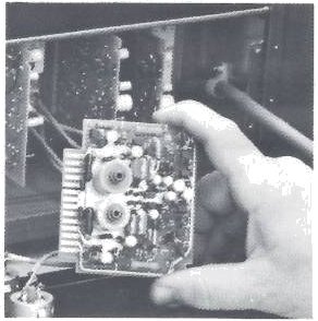 A hand holding a plug-in audio card from the MX-5050-8 electronics, its gold-plated edge connector at the left