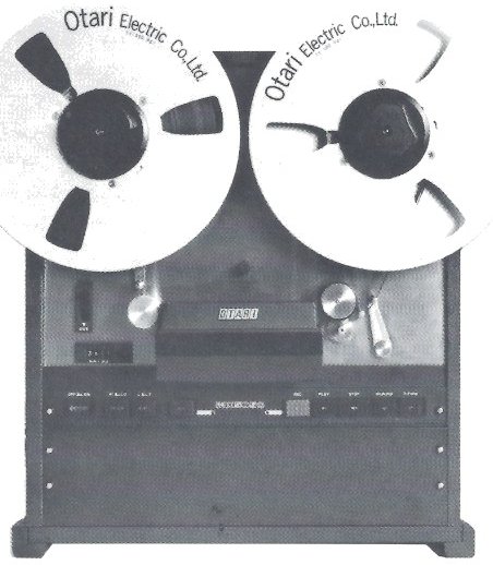 The MX-5050-8 transport photographed straight on, both reels fitted, with the push-button row and the empty lower panel of its case below the deck plate